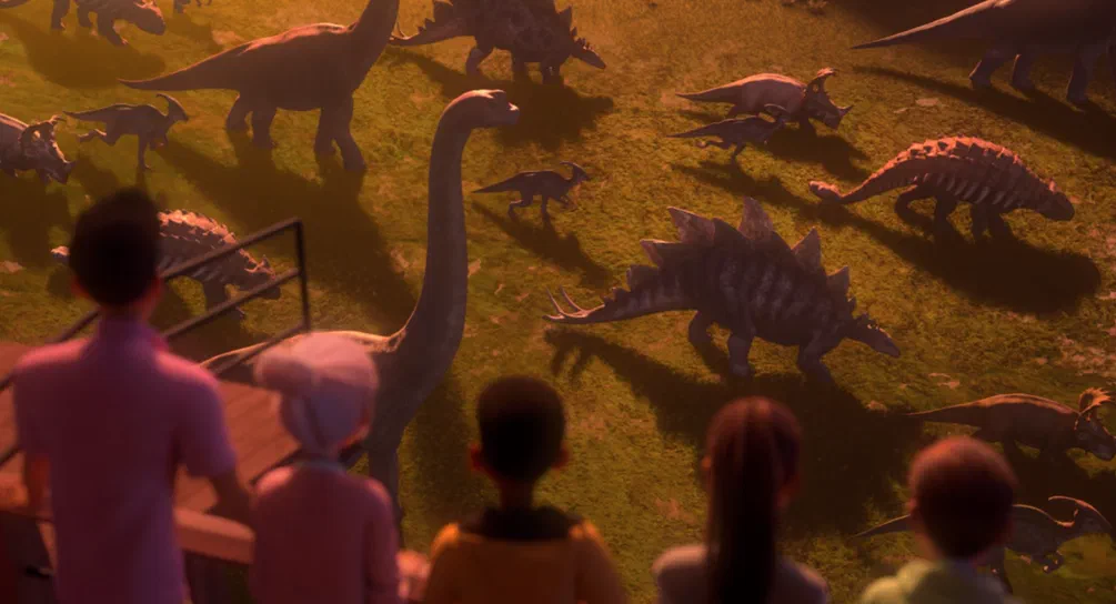 Des dinosaures animés dans une prairie ensoleillée observés par des enfants, scène du jeu vidéo Jurassic World Camp Cretaceous.