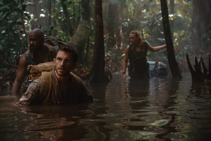 Trois personnes marchent en eau jusqu'à la poitrine au milieu d'un environnement de jungle luxuriante, rappelant une scène de Jurassic World Rebirth.