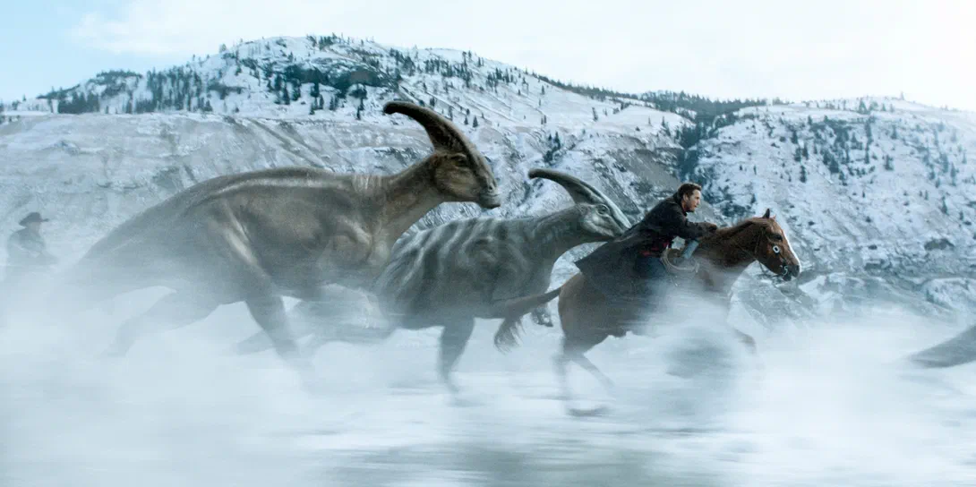 Dans un paysage enneigé et brumeux, Chris Pratt chevauche une monture poursuivi par deux dinosaures à cornes.