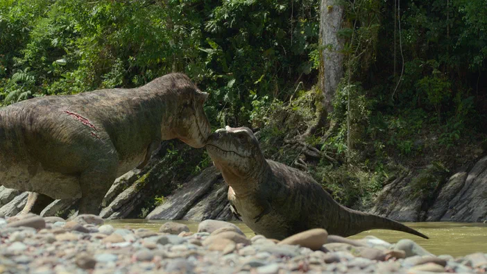 Deux Tyrannosaures se touchent le museau dans un environnement de forêt.